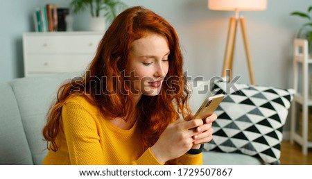 Happy and positive girl sitting on sofa at home and using smartphone.