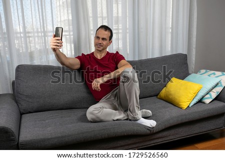 Mature man (44 years old) sitting on the couch, wearing socks and taking a picture of himself.