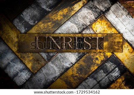 Photo of real authentic typeset letters forming Unrest text on vintage textured grunge copper and black background 
