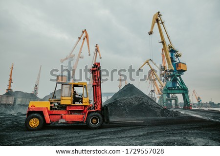 Heavy duty forklift truck parked near huge pile of coal. Dock distribution center