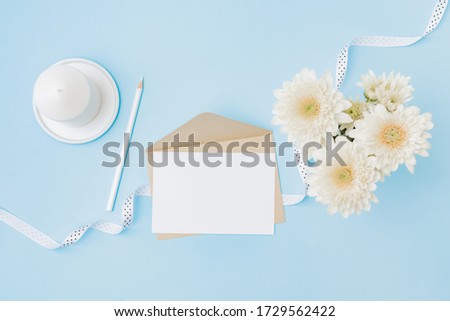 Mockup white wedding invitation and envelope with flowers in a vase on a blue background