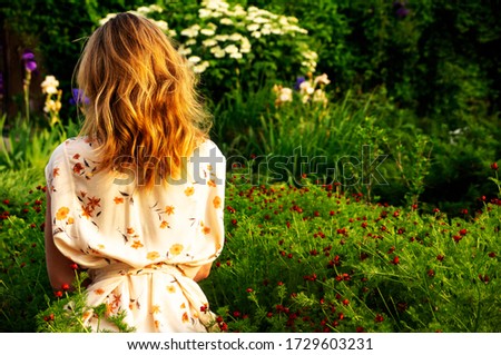 A girl sits with her back in a blooming garden. Back view.