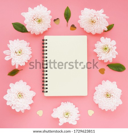 
a light yellow notebook on a spring and light pink chrysanthemum flowers in a circle on a pink background. space for text.
