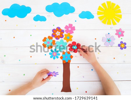 Composition of colorful flowers, sun, clouds from multi-colored paper, step by step. Tree of flowers. Child make crafts his own hands. DIY handmade art creativity on wooden table. Top view, copy space