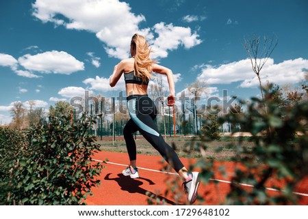 Girl runs on a treadmill on the street. Red running track. Blue sky . Street sport. Young athletic girl in leggings, sneakers and a top.