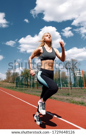 Girl runs on a treadmill on the street. Red running track. Blue sky . Street sport. Young athletic girl in leggings, sneakers and a top. Track and field athlete. Sport.