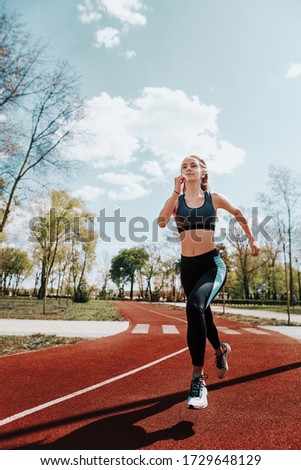 Girl runs on a treadmill on the street. Red running track. Blue sky . Street sport. Young athletic girl in leggings, sneakers and a top. Track and field athlete.