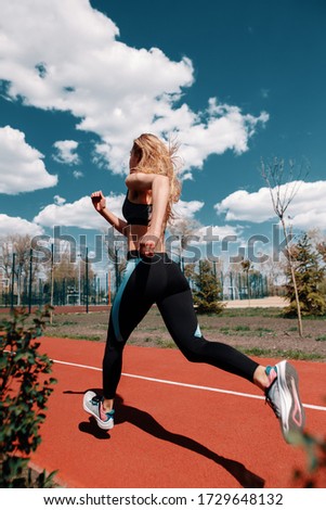 Girl runs on a treadmill on the street. Red running track. Blue sky . Street sport. Young athletic girl in leggings, sneakers and a top. Track and field athlete.