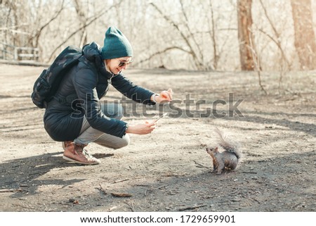 Caucasian woman taking picture photo of squirrel in park. Tourist traveler girl snapping smartphone photos of wild animal in forest. Fun outdoor activity and blogging vlogging online.