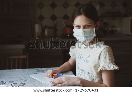 A girl in a protective mask draws with a pen in a sketchbook. Idea for quarantining a child