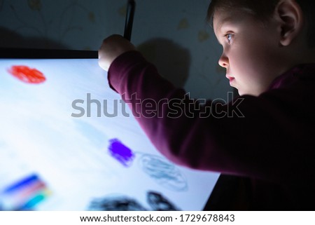 Little boy draw on a graphic tablet in the evening in a dark room under the light of the monitor. Creative education concept. Close up view.
