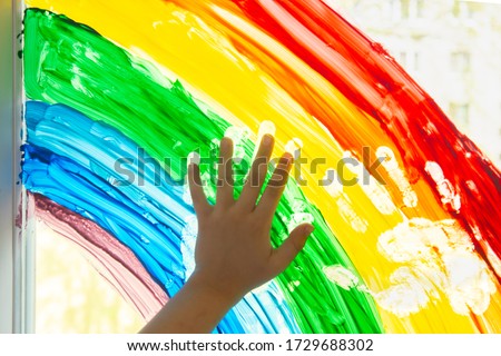 Children's hand touches painting rainbow on the window. Stay at home during coronavirus pandemic. Social media campaign for coronavirus prevention, chase the rainbow flashmob