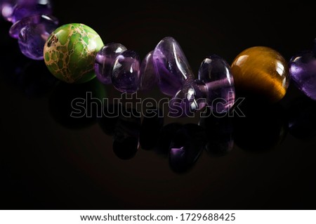 Balls of semiprecious stones on a leash with amethysts on a hand on a black background.