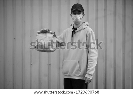 Courier with a parcel closeup. The courier delivers food home. Quarantine food delivery. Against a neutral background, the courier transfers the package / order to the recipient. Black and white photo