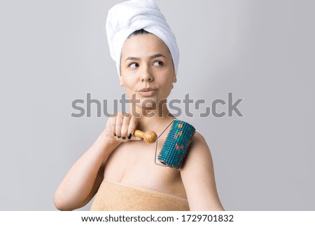 Brunette with a towel on her head using roller for face massage isolated on grey background
