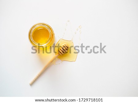 glass jar with honey and with a wooden honey stick on a white background. a honey stick lies on a white table with honey dripping from it on the table. healthy eating concept. flat lay. copy space.