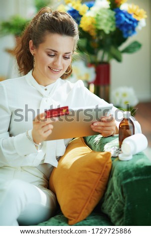 modern middle age housewife in white blouse with credit card and empty medicine bottle ordering drugs online on a tablet PC in the modern living room in sunny day.