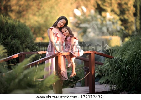 Mother and daughter are hugging on a wooden bridge in the park.
Image with selective focus, noise effects and toning. Focus on the girl and women.