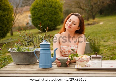 concept of Breakfast and teatime in open air. girl drinks tea from vintage teapot and mug (inscription on French: good coffee to start with, I have good day) picnic in countryside. Provence France.