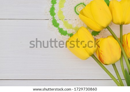Natural yellow tulips and a knitted napkin lie on a light white wooden background. Background, texture, and decoration, label stock.
