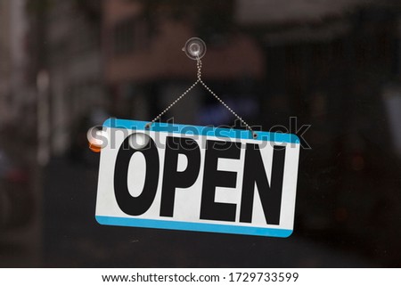 Close-up on a blue open sign in the window of a shop displaying the message "Open".
