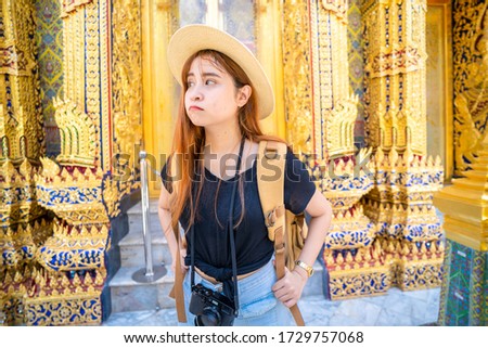 Cute Asian women carrying backpacks, and cameras, She is traveling in a temple in Bangkok of Thailand. She is looking for something.