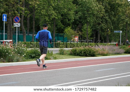 A man in a blue and baseball cap runs on a track in a city park.
