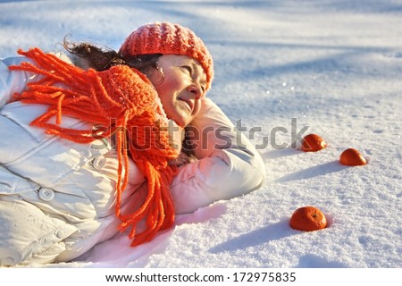   A european woman lying on the snow with tangerines around her