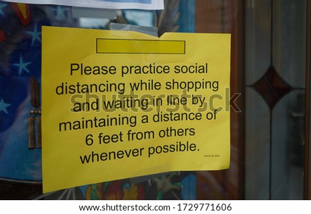                       yellow sign in store window asking patrons to practice social distancing while shopping          