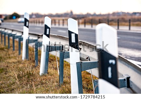 Black and white signal road posts on an asphalt road. Country road and fence.