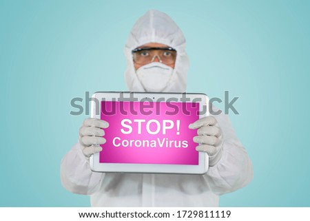Doctor showing text of stop coronavirus on digital tablet while wearing hazmat suit in the studio