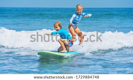 Happy baby boy and girl - young surfers ride with fun on one surfboard. Active family lifestyle, kids outdoor water sport lessons, swimming activity in surf camp. Sea beach summer holiday with child. Royalty-Free Stock Photo #1729884748