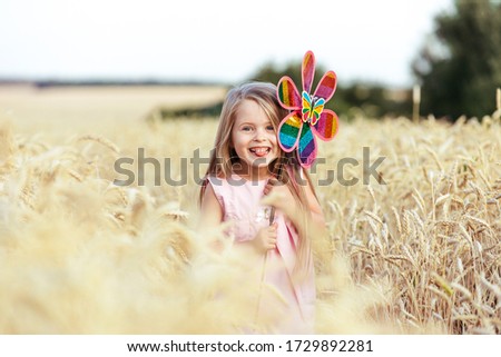 Happy girl holding wind toy running in wheat field, rejoicing life, happiness