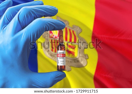 Andorra flag with Coronavirus Covid-19 concept. Doctor with blue protection medical gloves holding a vaccine bottle. Epidemic Virus, Cov-19, Corona virus outbreaking.