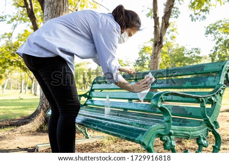 Asian woman wear medical mask using spraying alcohol,disinfectant spray on bench,wiping the dirt,during the pandemic of Covid-19,Coronavirus,cleaning,disinfecting wipe the public bench at outdoor park