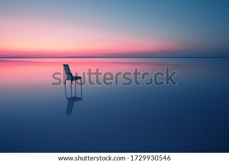 Chair among smooth water of lake at the sunset. The concept of solitude and unity with nature. A chair stands in the water of the Salt Lake Ace. Anatolia, Turkey Royalty-Free Stock Photo #1729930546