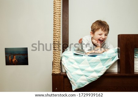 The boy laughs as he reads the book. On his bed. Upper floor