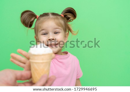little girl 4 years old in a pink T-shirt on a green background with enthusiasm reaches out to ice cream, happy eyes