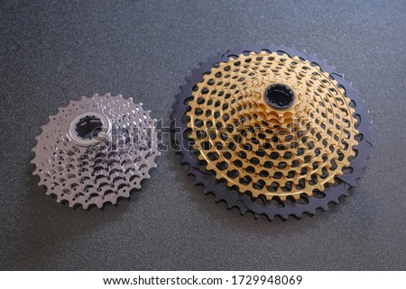 Rear mountain bike cassette, size comparison 12-speed vs 8-speed, big and small, in silver and golden color, the big 12-speed one is a 10-50 teeth