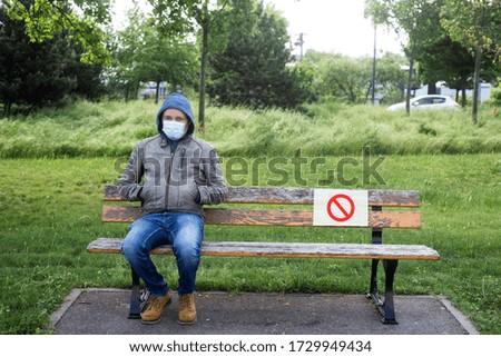 Portrait of  man sitting on wooden bench in urban park with a forbidding sign on paper - Social Distancing  concept 