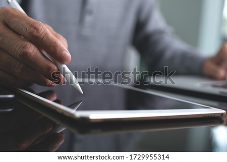 Multitasking business man hand using digital tablet, laptop computer and mobile smart phone, connecting internet in modern office. Graphic designer with stylus pen working on tablet on table, close up