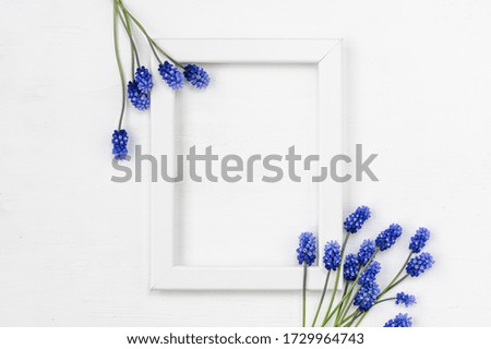 White wooden frame and a bouquet of blue flowers on a white background. Top view. Flat lay.