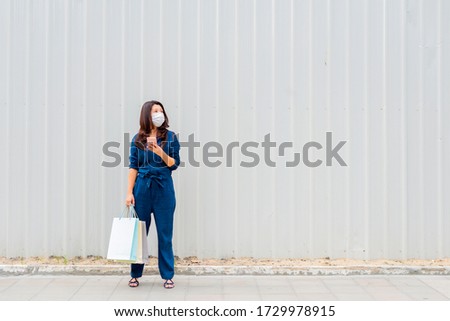 Asian woman in city shopping street. Woman wearing face mask using smartphone to network outdoors. Tourist woman using technology, travel lifestyle. 