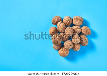 Heap of whole ripe walnuts on blue background. Copy space. Top view