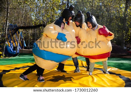 Portrait of happy excited men and women dressed as sumo wrestlers on inflatable arena