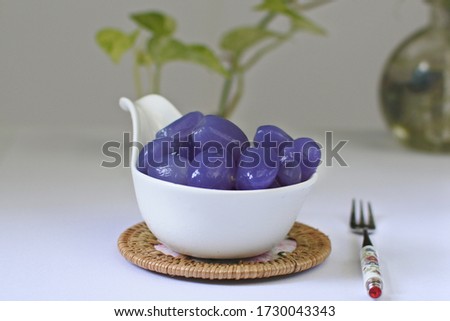 Indonesian dessert known as manisan kolang-kaling , made from palm fruit and sugar, coloured purple by using butterfly pea flower. Served on white table, and white background.