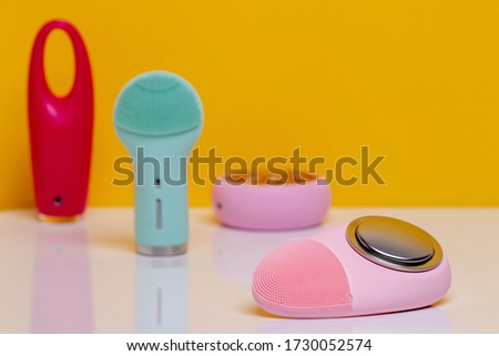 Beauty and skincare concept. Selective focus on a modern pink electric face cleansing silicone brush with massage sonic vibration on a white table and three further blurred electric beauty treatment.