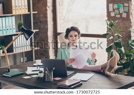 Photo of attractive business boss lady notebook table distance home remote work hold papers documents legs on table confident chief sit chair modern interior office indoors