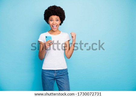 Photo of crazy beautiful dark skin wavy lady holding telephone hands astonished with many new followers subscribers wear casual white t-shirt jeans isolated blue color background