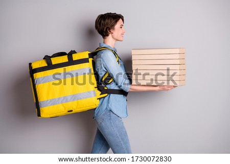 Profile side photo of positive worker girl courier work covid-19 quarantine hold pizzeria boxes deliver house home go walk copyspace wear denim jean shirt isolated gray color background